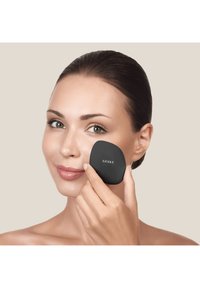 Svart makeup-applikator, ovalformad med slät yta, märkt "GESKE," som används på en persons kind mot en neutral bakgrund.