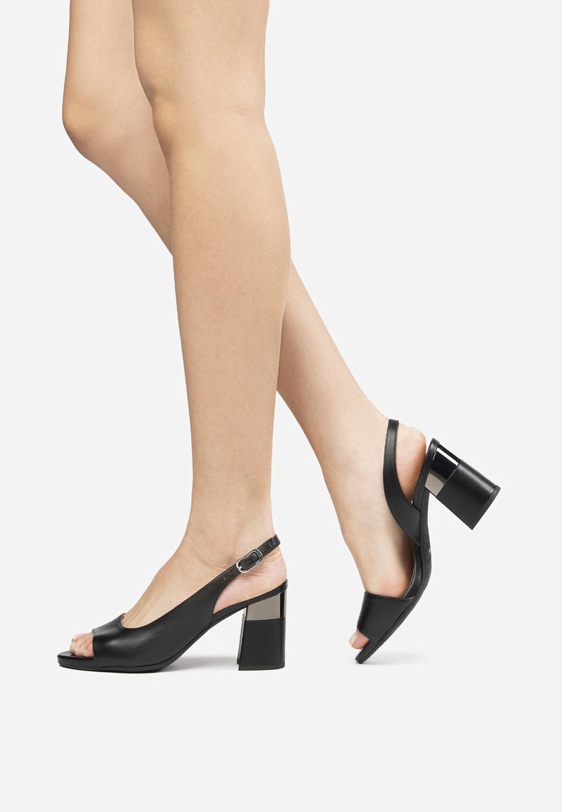 Tacchi slingback aperti neri in pelle, con tacco chunky, cinturino alla caviglia regolabile e un accento metallizzato lucido sul tacco.