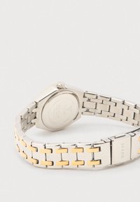 Sølvfarvet ur i rustfrit stål med et armbånd med gyldne accenter, oktagonet urkasse og en glat finish. Har urskive og krona synlige.