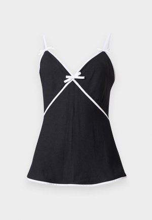 Femme portant un haut sans manches noir avec bordure blanche et un pantalon à jambes larges avec un imprimé graphique multicolore représentant divers logos de marques.