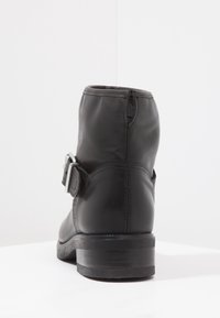 Botín negro de cuero hasta el tobillo con puntera redonda, cremallera lateral y detalle de hebilla plateada. Presenta un tacón bajo y apilado y una textura suave.