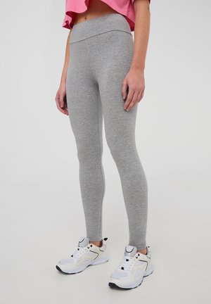 Leggings grigi realizzati in un tessuto elastico, con design a vita alta e una texture liscia; abbinati a scarpe da ginnastica bianche.