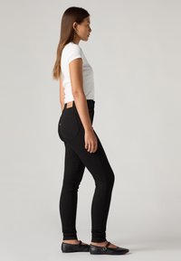 Black skinny jeans made of denim, featuring a high waist and five-pocket design. Paired with a white fitted t-shirt and black flats.