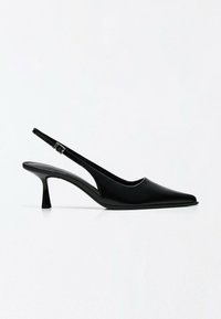 Chaussure slingback en cuir noir avec bout pointu et talon bas incurvé sur fond blanc uni.