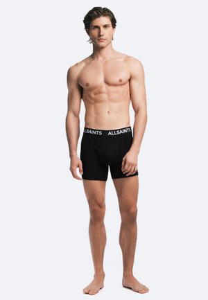 Black boxer shorts with a branded waistband, made of a smooth fabric. They feature a form-fitting design with an elasticated waist.
