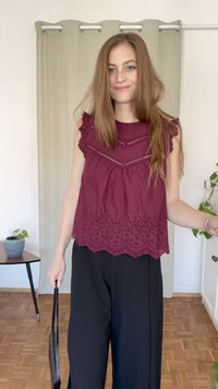Top sem mangas bordô com detalhes bordados e bainha recortada, combinado com calças largas pretas. Modelo segurando uma bolsa preta.