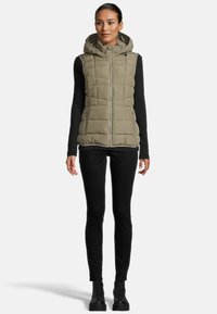 Gilet matelassé vert olive avec une fermeture éclair sur le devant, une capuche et deux poches latérales, porté sur un haut noir à manches longues côtelé et un pantalon noir.
