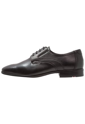Chaussure habillée en cuir noir avec une finition lisse, lacets, accents cousus, et une semelle en caoutchouc plate. Présente un panneau latéral texturé.