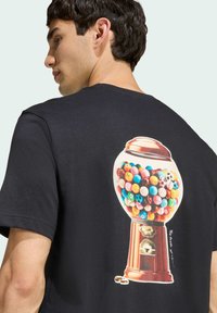 Černé tričko s barevným grafickým motivem kuželky na zadní straně. Jasné, kulaté žvýkačky a detailní design stroje.