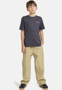 Camiseta gris con pequeño logo de "Element", combinada con pantalones holgados de color beige claro y zapatillas negras. Diseño simple y casual, con ajuste cómodo.