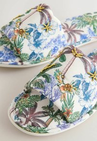 Gėlėtu raštu margintos lengvai užsimaunamos sandalės su žaliais, mėlynais ir oranžiniais tropiniais raštais, puoštos mažomis auksinėmis karoliukų detalėmis.