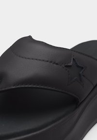 Μαύρο σανδάλι με λωρίδα μαξιλαριού που διαθέτει ραμμένη περικοπή αστεριού και παχύ μαξιλαρωμένο πέλμα σε λευκό φόντο.