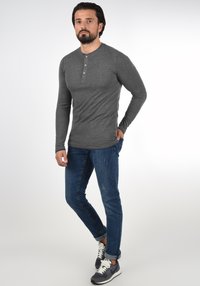 Szürke hosszú ujjú henley póló, három gombos gombolással, sötétkék slim fit farmernadrággal és szürke sportcipővel párosítva. Simá szövet, laza dizájn.