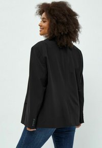 Blazer nero con un design su misura, realizzato in tessuto liscio. Presenta maniche lunghe, rever a punta e uno spacco posteriore singolo.