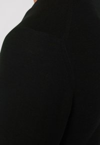 Schwarzer Strickpullover mit strukturierter Oberfläche, nahtlosem Schulterdesign und figurbetonter Silhouette. Das Material bietet leichte Dehnbarkeit.