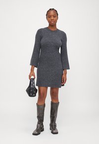 Robe-sweater côtelée grise avec de longues manches en cloche, associée à un sac à main noir avec des accessoires ronds et des bottes grises jusqu'aux genoux.