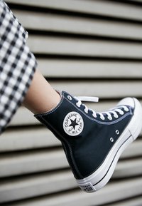 Wysokie trampki Converse w granatowej kanwie z białą gumową podeszwą i sznurówkami. Posiadają charakterystyczne okrągłe logo z boku. Teksturowana tkanina.
