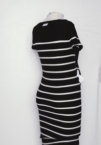 Robe rayée noire et blanche en tissu côtelé ; design ajusté avec des manches courtes ; étiquette visible à l'arrière ; longueur au genou avec détails latéraux.