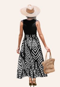 Haut sans manches noir avec une jupe maxi à motif chevron noir et blanc, accentuée par un ourlet à volants et associée à un sac en paille tissé.