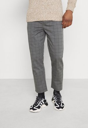 Pantalons à carreaux gris avec une coupe slim et un ourlet retroussé, associés à des chaussures de sport noir et blanc avec une surface texturée et des lacets.