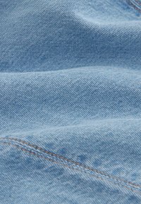 Tissu en denim bleu clair à la texture douce, présentant un motif tissé subtil et des coutures visibles en orange contrasté. Apparence froissée.