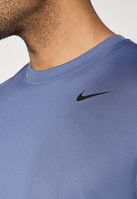 Μπλε κοντομάνικο μπλουζάκι από λείο ύφασμα, με μαύρο λογότυπο Nike swoosh στην αριστερή πλευρά του στήθους. Σχεδίαση με στρογγυλή λαιμόκοψη.