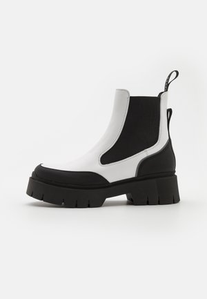 Stevige zwart-witte Chelsea-laars met dikke profielzool, elastische zijpanelen en trekbandjes op een witte achtergrond.