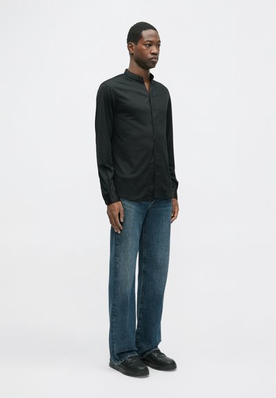 Mustat pitkät hiharat kauluspaidat, joissa on mandariinikaulus ja napit, yhdistettyinä löysiin sinisiin farkkuihin ja mustiin lenkkareihin. Yksinkertainen muotoilu, sileä rakenne.