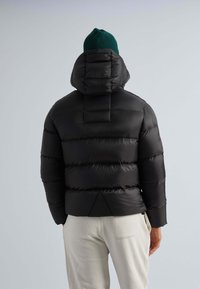 Schwarze Steppjacke mit Kapuze, mit gesteppten Abschnitten und glatter Textur. Kombiniert mit hellen Hosen; minimalistischem Design.