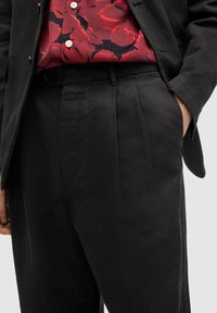 Black linen trousers with front pleats and side pockets, paired with a red floral patterned shirt featuring light buttons.