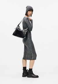 Γυναίκα που φοράει γκρίζο πλεκτό φόρεμα, ταιριαστό σκουφί, μαύρες δερμάτινες μπότες και κρατάει μαύρη δερμάτινη τσάντα ώμου στον έναν ώμο.