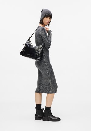 Egy nő szürke, bordázott ruhát visel, illő sapkával, fekete bőr csizmával, és egy fekete bőr oldalántáskával az egyik vállán.