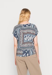 Blouse à manches courtes en tissu bleu présentant un motif mixte floral et géométrique, avec des couleurs contrastées et une texture douce.
