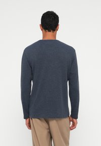 Ilgi piedurkņu tumši zila T-krekls, izgatavots no mīkstas teksturētas šķiedras. Tam ir apaļš kakla izgriezums un brīvs griezums, attēlots no aizmugures.