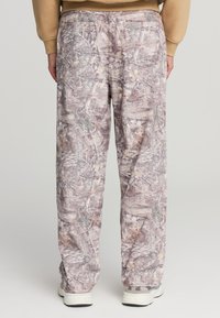 Pantaloni in stampa camouflage che presentano un mix di marroni, verdi e beige; vestibilità ampia con un design a gamba dritta e due tasche posteriori.