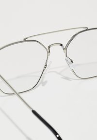 Gafas de sol de montura metálica con forma octogonal, que cuentan con almohadillas nasales transparentes, un puente doble y patillas delgadas en color negro.