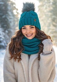 Gorro de punto en color teal con un pom-pom de piel, bufanda a juego en teal y abrigo de forro polar beige. Manoplas de punto en color gris claro. Fondo brillante y nevado.