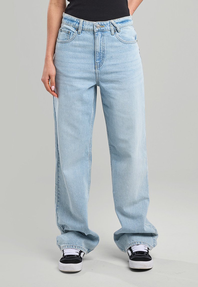 Light blue high-waisted jeans with a relaxed fit, featuring a button and zipper closure, five pockets, and a frayed hem. Paired with black sneakers.