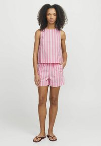 Růžový pruhovaný bezramínkový top a odpovídající šortky vyrobené z lehkého materiálu. Mezi nápadnými detaily jsou boční kapsy a uvolněný střih.