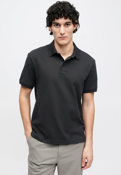 Melna polo krekls ar smalku zvīņveida rakstu, īsām piedurknēm un apkakli. Izgatavots no teksturēta auduma, ar pogu pie kakla.