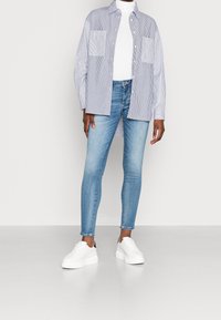 Camisa de botones a rayas en azul y blanco, combinada con jeans skinny azul claro y zapatillas de plataforma blancas. Textura suave, diseño casual.