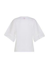 Camisa blanca de manga ancha con escote redondo y una pequeña etiqueta rosa en el centro superior de la parte trasera.