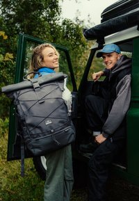 Roll-top backpack in dark gray, made of water-resistant material, featuring an adjustable strap, zippered pocket, and elastic cord detailing.