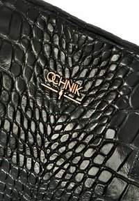 Czarna torebka kopertówka z sztucznej skóry o fakturze krokodyla. Posiada złote metalowe logo wytłoczone na przodzie. Gładkie i błyszczące wykończenie.