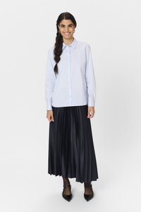 Ljusblå skjorta med knäppning och långa ärmar, kombinerad med en plisserad svart maxikjol. Outfiten kompletteras med spetsiga svarta skor.