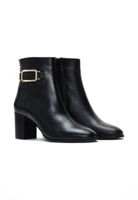Bottines noires en cuir avec un bout pointu, un talon carré, une fermeture éclair sur le côté et un accent en boucle dorée sur la cheville extérieure.