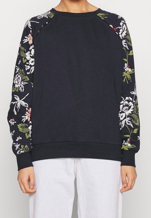 Donkerblauwe sweatshirt met bloemenpatroon op de mouwen in wit, roze en groen. Geribbelde hals en manchetten. Zacht materiaal met een ontspannen pasvorm.