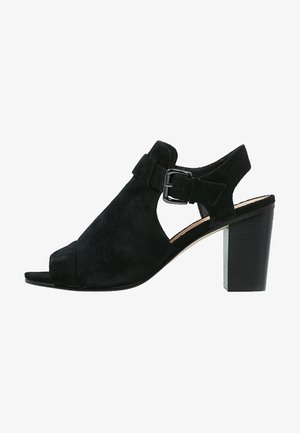 Sandales à talons ouverts en suède noir avec une sangle à boucle et un haut talon carré, dotées d'un design découpé sur les côtés.