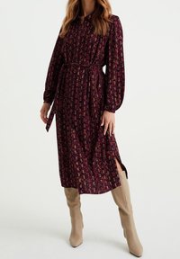 Lång burgundy klänning med knappstängning, blommönster, bandad midja med knyt och sidoklyftor. Bärs med beige knähöga stövlar.