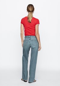 Rotes Kurzarm-T-Shirt, kombiniert mit hellblauen High-Waist-Jeans aus Denim, mit geradem Bein und Gesäßtaschen, von hinten gezeigt.